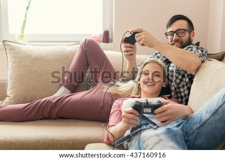 Couple in love enjoying their free time, sitting on a couch next to the window, playing video games and having fun. Lens flare effect on the window