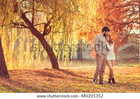 Young couple in love holding hands and walking through a park on a sunny autumn day