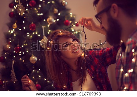 Beautiful young couple in love decorating Christmas tree, arranging the christmas lights and having fun