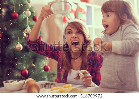 Mother and daughter making Christmas cookies and having fun. Mother sifts the flour through a sieve on the great amazement of her daughter