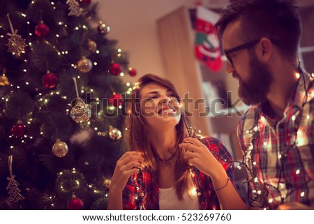 Beautiful young couple in love decorating Christmas tree, arranging the christmas lights and having fun