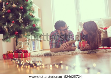 Beautiful young couple lying on the living room floor next to a nicely decorated Christmas tree, exchanging Christmas presents