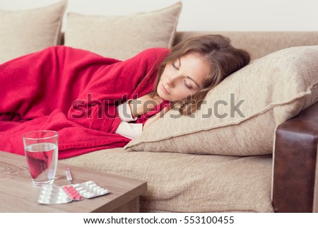 Sick woman covered with a blanket lying in bed with high fever and a flu. Pills and glass of water on the table