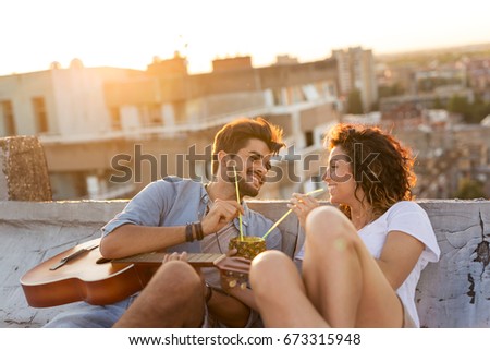 Young couple in love drinking a pineapple cocktail and having fun at rooftop party in sunset. Focus on the guy