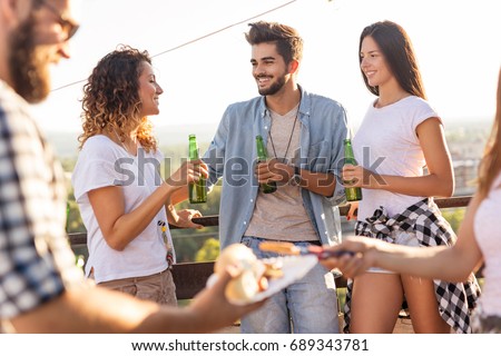 Group of young friends having fun at rooftop party, drinking beer, eating barbecue and enjoying hot summer days. Focus on the couple on the right