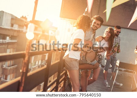 Friends having fun at rooftop party, playing the guitar and singing. Focus on the guy playing the guitar
