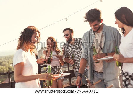 Group of young friends having fun at rooftop party, making barbecue and enjoying hot summer days. Focus on the couple in the background