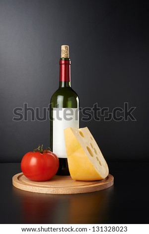 Red vine bottle with cheese and tomato on wooden cutting board