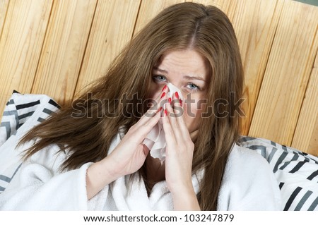 Photo of sick woman sitting in bed with tissue and blowing her nose into it