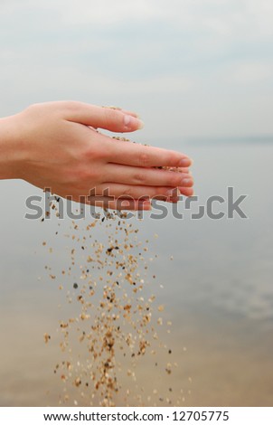 falling sand in female hands over sea