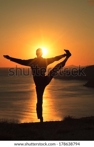 Man balance in yoga tree pose on ocean beach at sunset