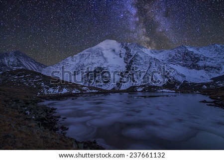 Magic night landscape with mountains, frozen lake and amazing starry sky.