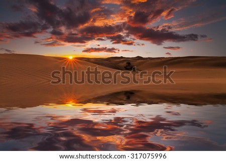 Reflection of the sunset sky and sand dunes in the water.