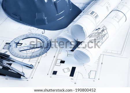 Engineer workplace with blueprints, compass, pen, protractor  and safety helmet
