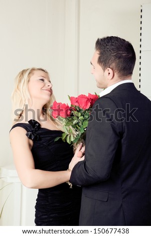 Loving young couple smiling at each other over a large bouquet of red roses as they stand looking into each others eyes