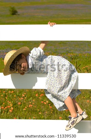 Little girl climbs white fence to get into meadow with flowers