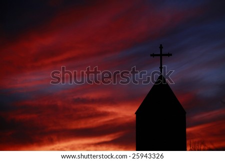 Holy cross on church against turbulent glowing red sky