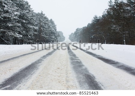 The asphalted road covered with snow. On road some strips from wheels of cars are visible