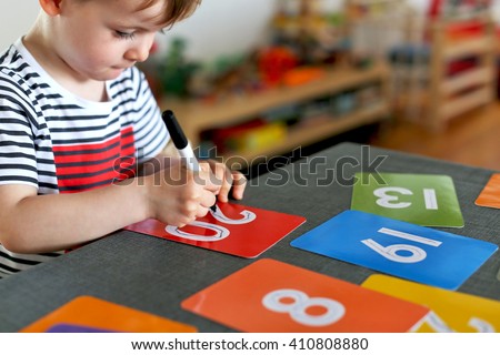 Picture of a young boy learning to write numbers on colorful cards with a focus on his hand and his pen