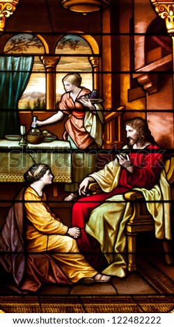 Stained glass window depicting visit of Jesus to home of Martha and Mary, with Mary sitting at feet of Jesus and Martha doing housework