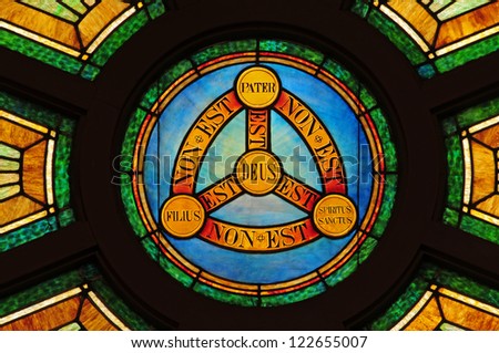 Stained glass window depicting doctrine of the Holy Trinity in Latin with symbols of circle and triangle