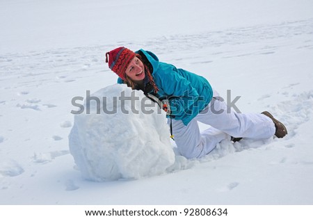 Young college-age woman rolling giant snowball to make snowman
