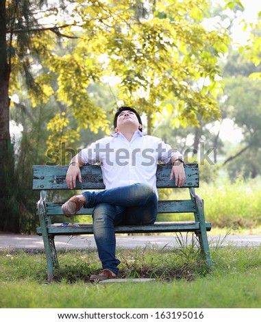 The young man sits on a bench in park