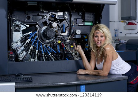 A cute looking blonde woman servicing a digital printing press, gets covered in grease and ink.