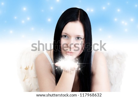 Young blackhaired woman with angel wings blowing some stars on blue background