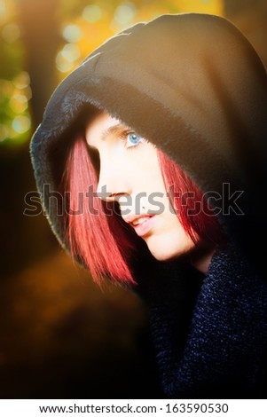 Head and shoulders portrait of a beautiful redhead woman with blue eyes standing in profile outdoors wearing a hooded anorak