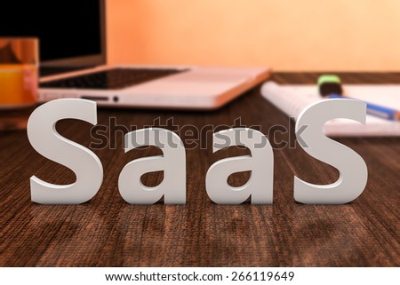 SaaS - Software as a Service - letters on wooden desk with laptop computer and a notebook. 3d render illustration.