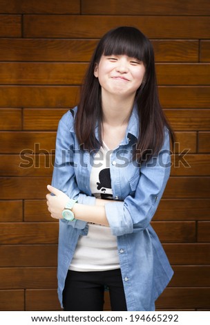 Portrait of young smiling asian teen standing with folded hands and big smile by the wooden wall Portrait of young smiling asian teen standing with folded hands and big smile by the wooden wall