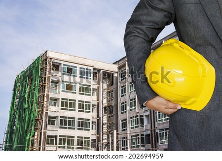Engineer hand holding yellow helmet for workers security against the background of  building under construction