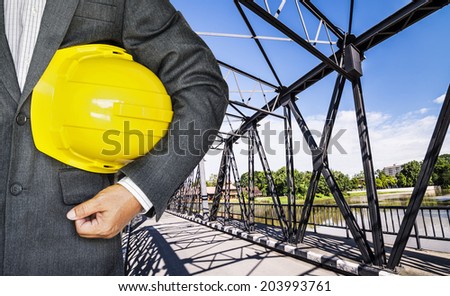 Engineer hand holding yellow helmet for workers security against historical railway bridge over the ping river ,Chiang Mai- Thailand.