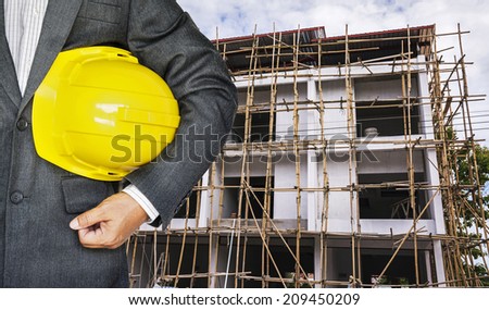 Engineer hand holding yellow helmet for workers security against the background of building under construction