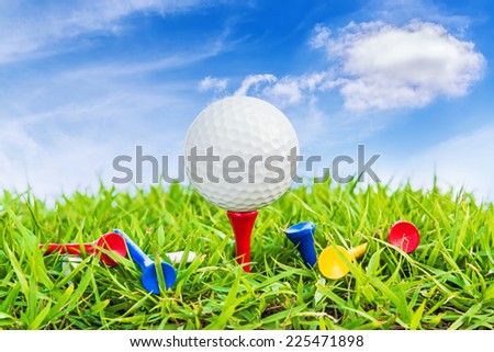 Golf ball on a tee against a blue sky and white clouds.