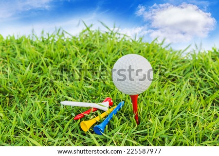 Golf ball on green grass against blue sky and white clouds