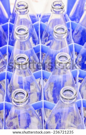Used glass bottles waiting for reuse in blue plastic crate.