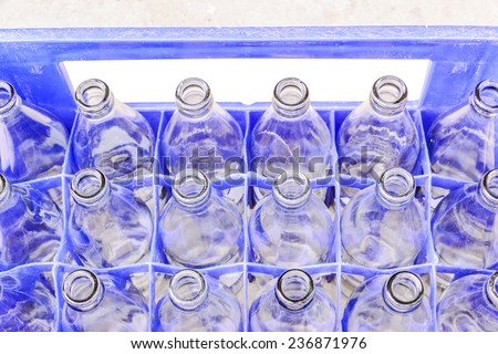 Used glass bottles waiting for reuse in blue plastic crate.