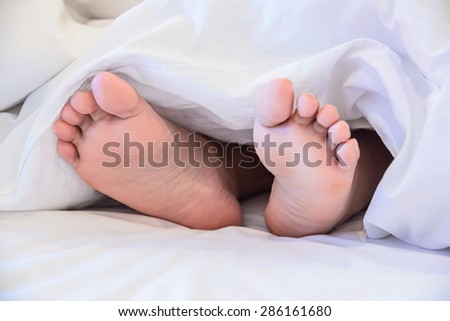 Close up of two feet in a bed against  white background.