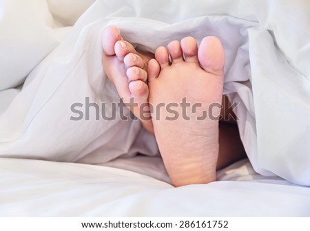 Close up of two feet in a bed against  white background.