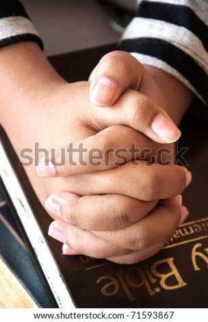 Young girls hands clasped in prayer over a Holy Bible
