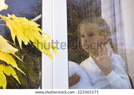Sad little girl watching through window at the rain