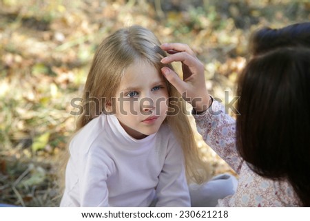 Mom gently stroking her daughter\'s head sitting in autumn park