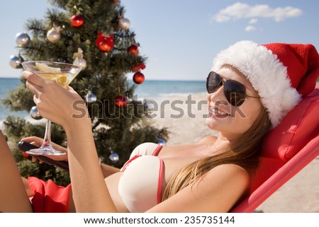 Santa girl in Christmas vacation on the beach with a glass of martini