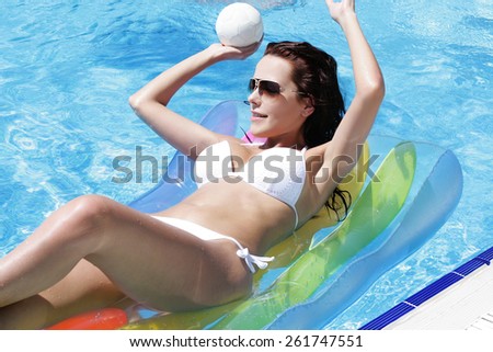Young woman in pool on a mattress with a ball