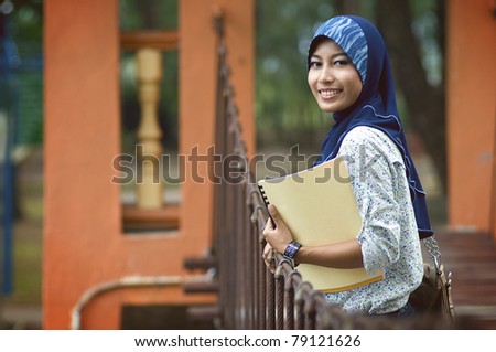 Beautiful young muslim lady smile while holding books at the bridge in the park