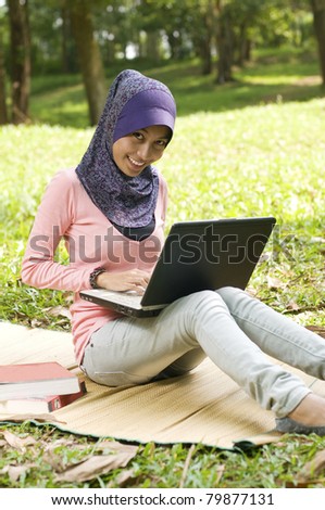 Beautiful young muslim lady typing on laptop while sit on the map in green garden