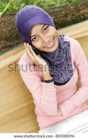 Beautiful young muslim lady smiling talk to the mobile phone isolated tree stump and green grass