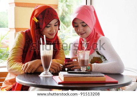 Beautiful muslim woman sharing reading information on mobile phone at a cafe with drinks and books on the table